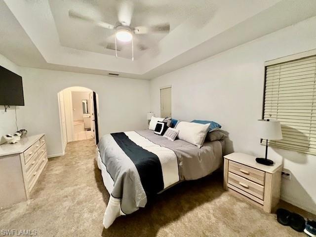 Bedroom featuring a tray ceiling, light colored carpet, arched walkways, and ceiling fan