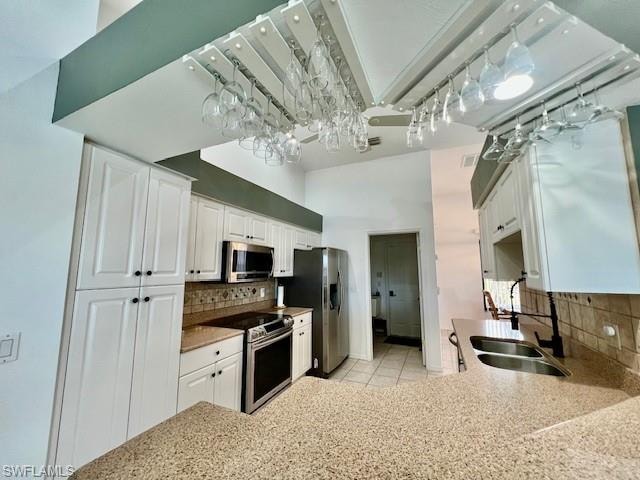 Kitchen with decorative backsplash, stainless steel appliances, white cabinetry, light stone counters, and light tile patterned floors