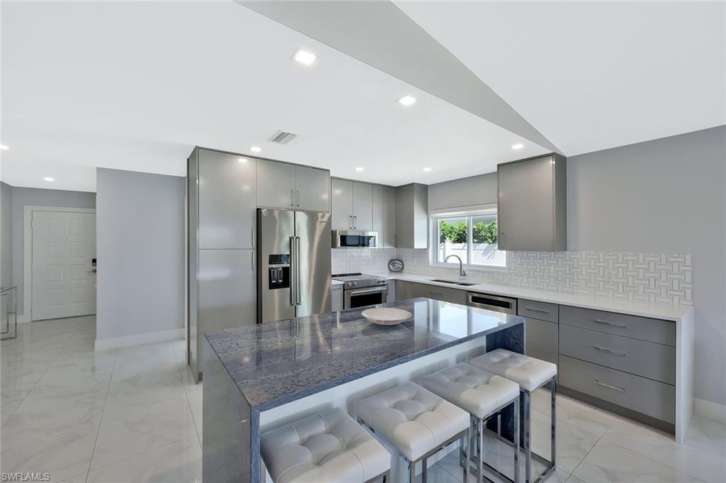 Kitchen featuring gray cabinetry, light marble finish flooring, backsplash, stainless steel appliances, and dark stone counters