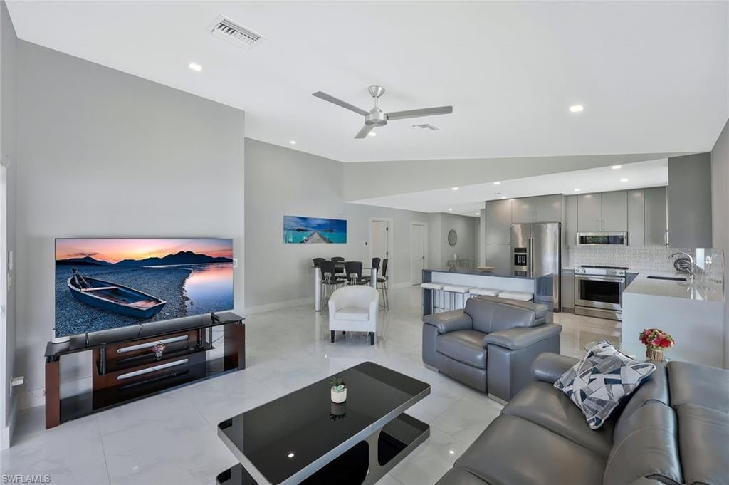 Living room with vaulted ceiling, ceiling fan, recessed lighting, and light marble finish flooring