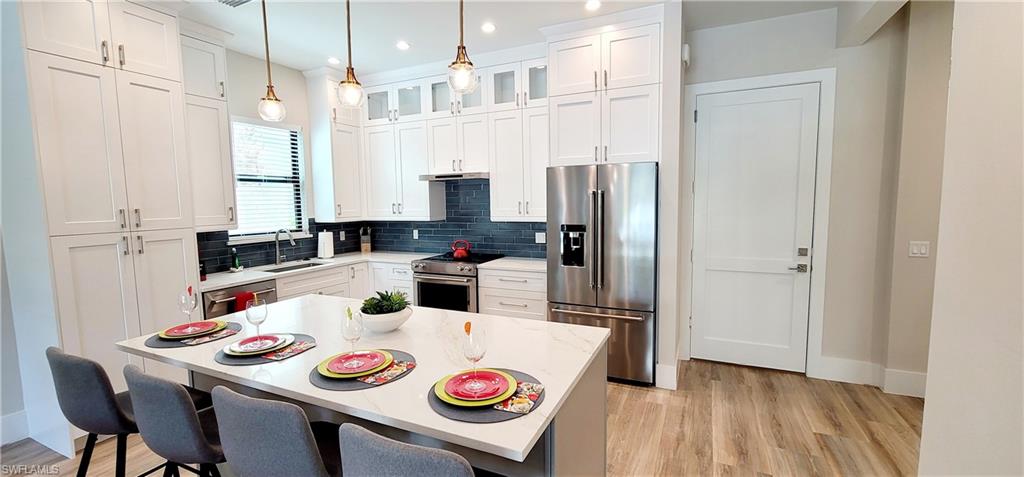 Kitchen with high end appliances, backsplash, hanging light fixtures, white cabinetry, and recessed lighting