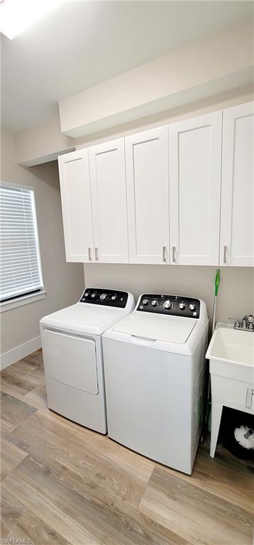 Laundry area with light wood-type flooring, cabinet space, and washing machine and clothes dryer