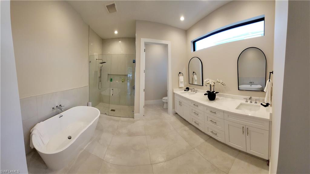 Full bath with a freestanding tub, double vanity, a stall shower, recessed lighting, and light tile patterned floors