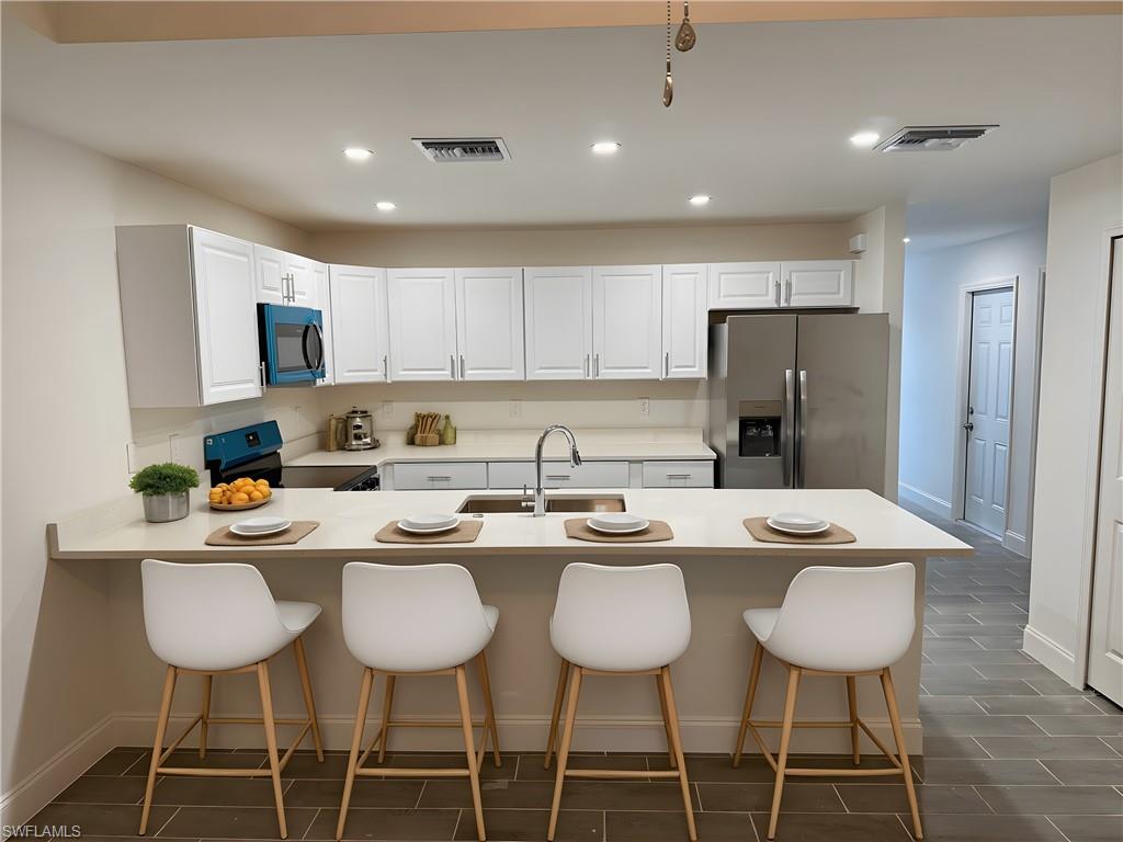 Kitchen featuring a kitchen bar, stainless steel refrigerator with ice dispenser, recessed lighting, range with electric cooktop, and a peninsula