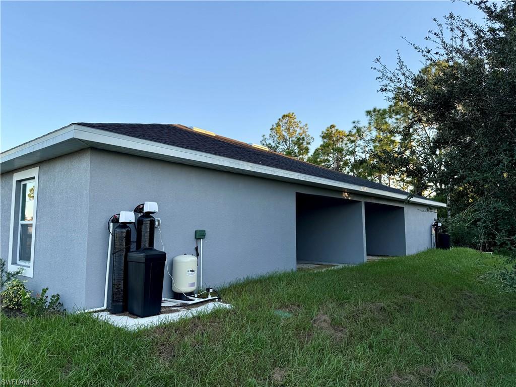 View of side of home with a yard, stucco siding, and roof with shingles