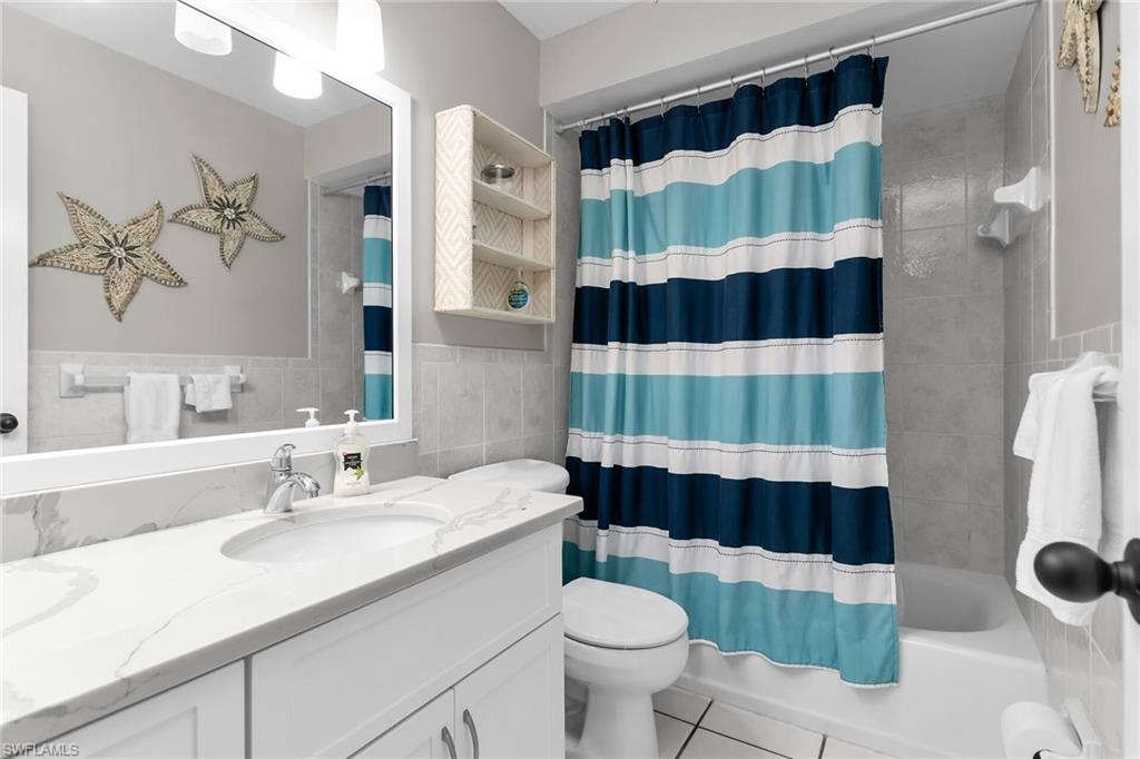Full bathroom with vanity, tile walls, light tile patterned floors, and shower / bathtub combination with curtain