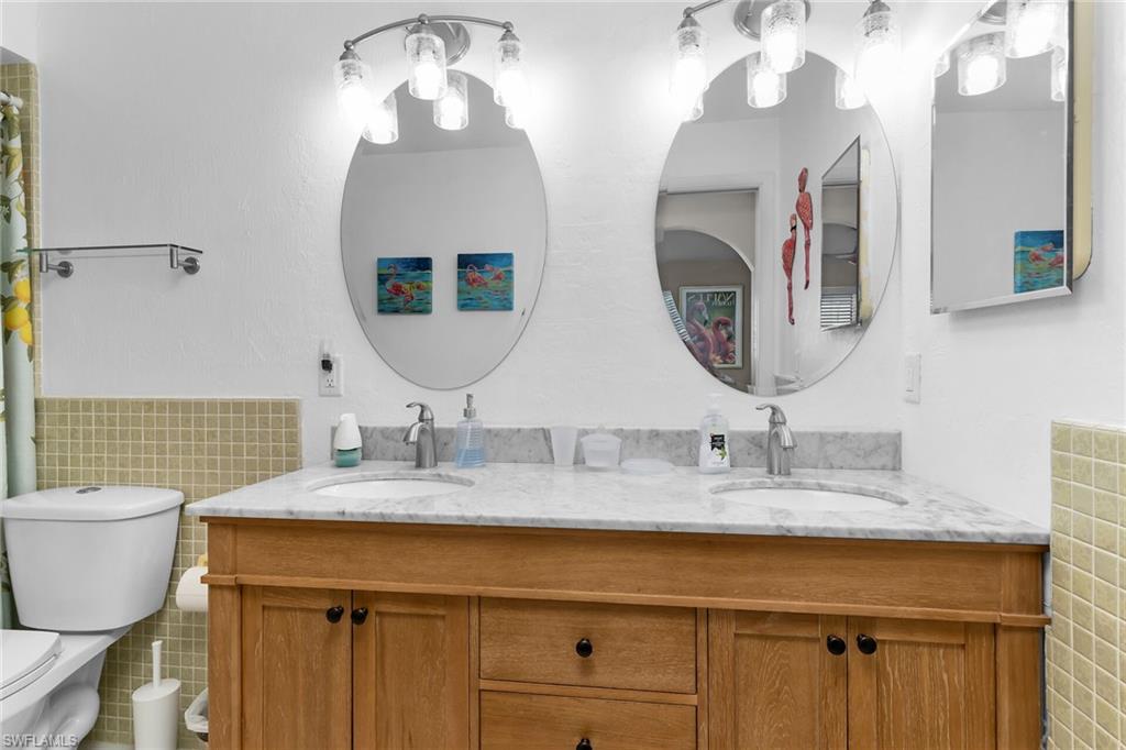 Full bathroom with tile walls, double vanity, and curtained shower
