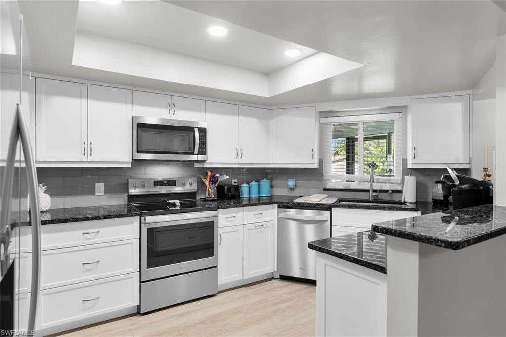 Kitchen with stainless steel appliances, dark stone countertops, white cabinets, a tray ceiling, and recessed lighting