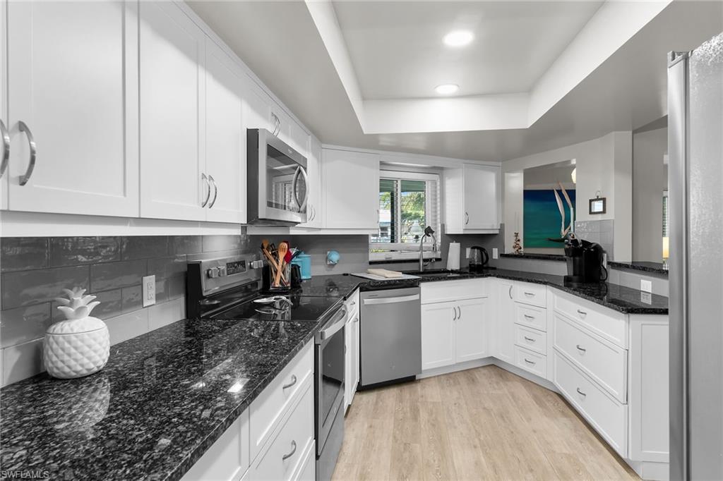 Kitchen featuring appliances with stainless steel finishes, dark stone counters, light wood finished floors, and white cabinetry