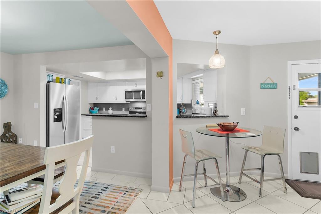 Kitchen with stainless steel appliances, white cabinetry, light tile patterned floors, hanging light fixtures, and dark stone counters