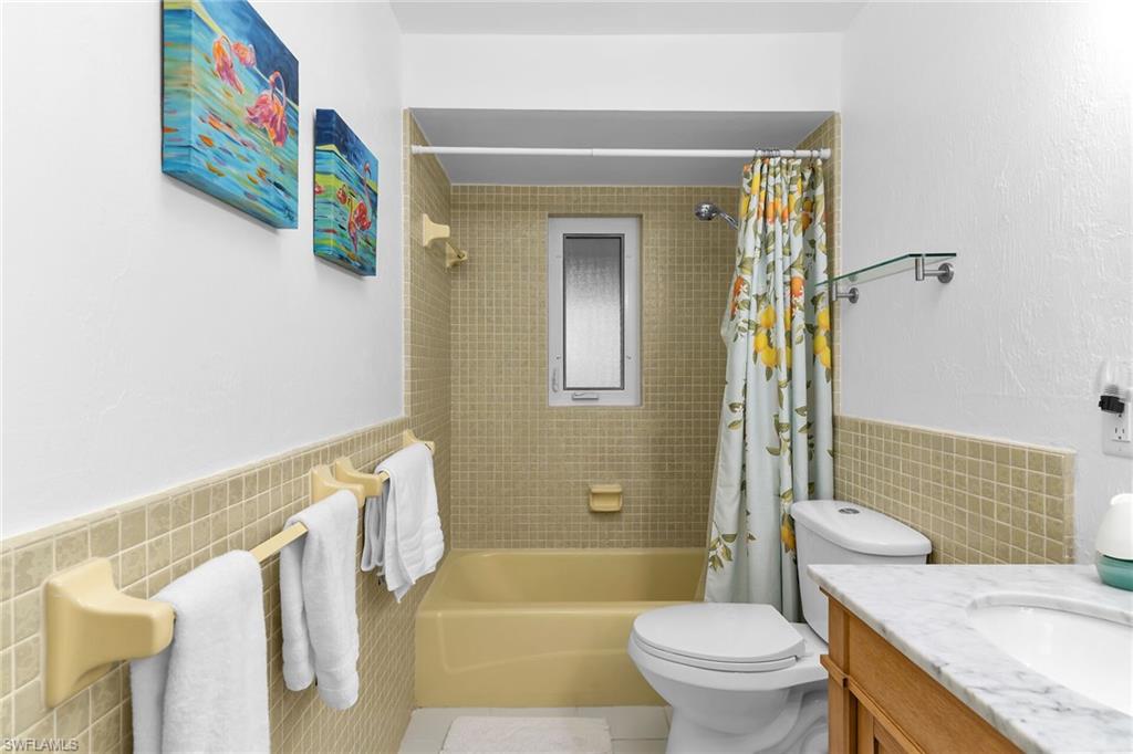 Bathroom with tile walls, shower / bath combination with curtain, vanity, wainscoting, and tile patterned floors