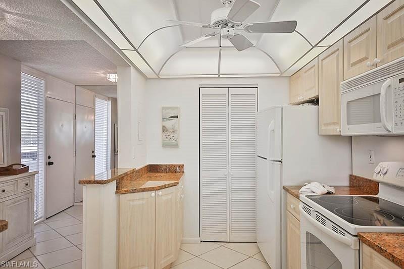 Kitchen featuring white appliances, light tile patterned floors, a ceiling fan, a peninsula, and a textured ceiling