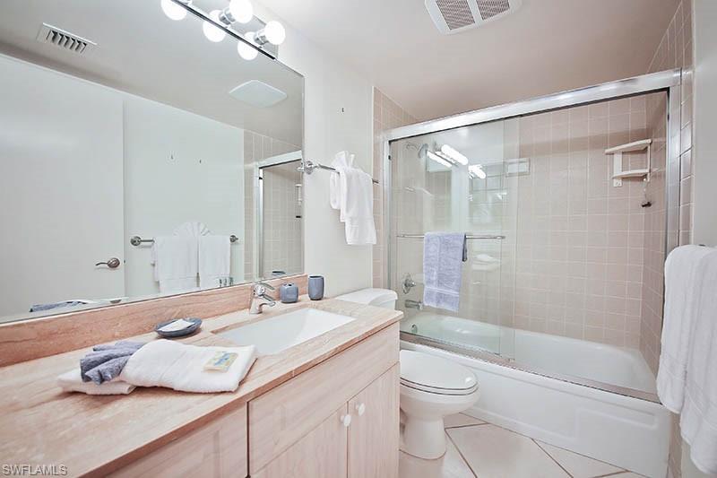 Full bathroom with bath / shower combo with glass door, light tile patterned floors, and vanity