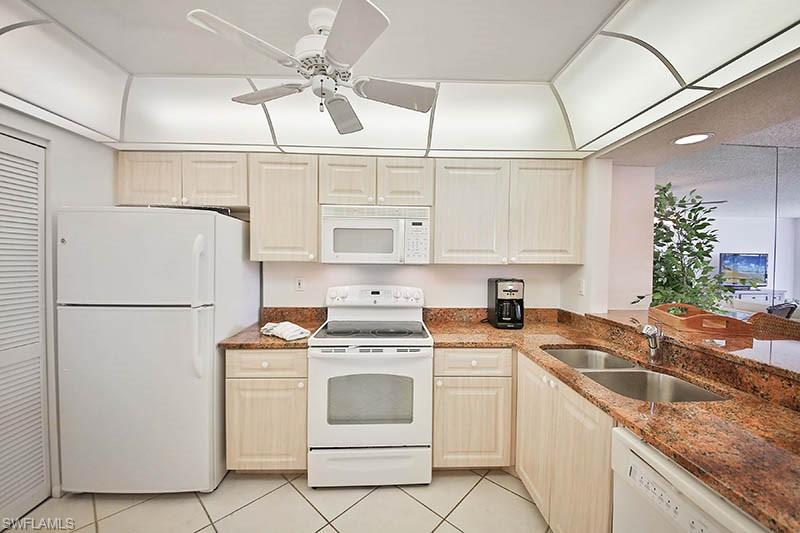 Kitchen with white appliances, light tile patterned flooring, dark stone countertops, recessed lighting, and ceiling fan