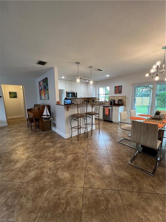 Kitchen featuring white cabinets, dark countertops, a kitchen breakfast bar, decorative light fixtures, and a peninsula