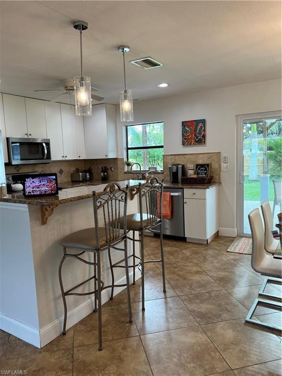 Kitchen featuring tasteful backsplash, a breakfast bar, white cabinets, decorative light fixtures, and dishwashing machine