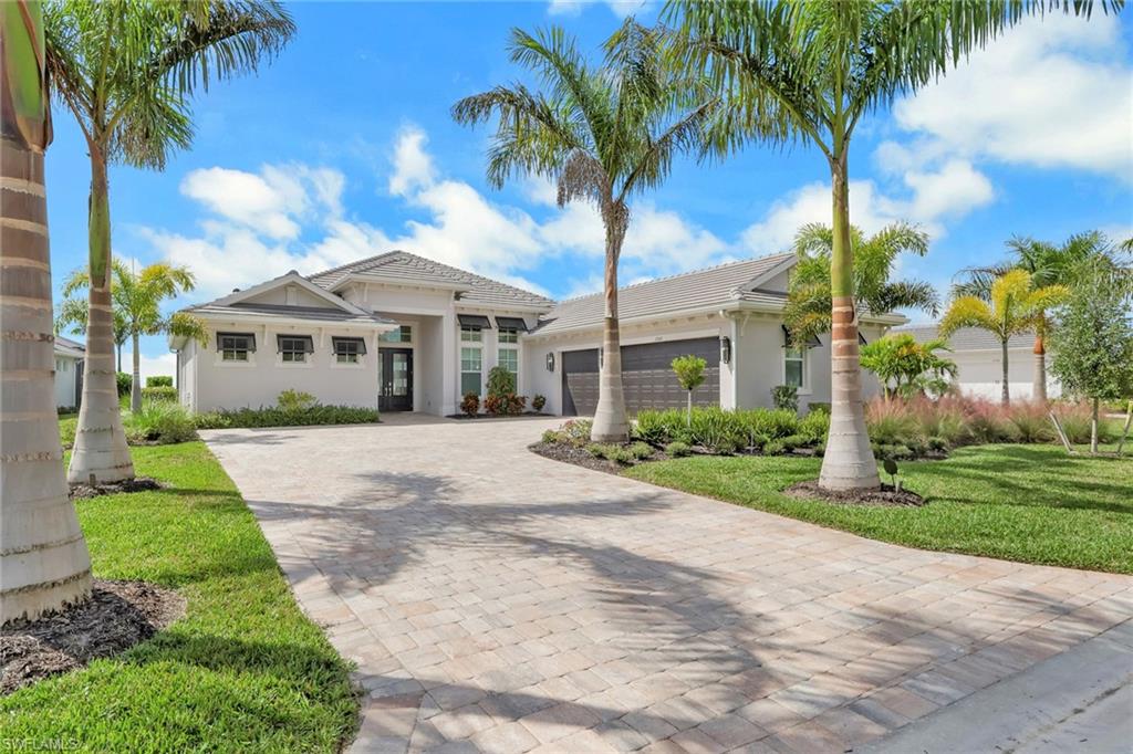 View of front of property featuring an attached garage, decorative driveway, a front lawn, and stucco siding