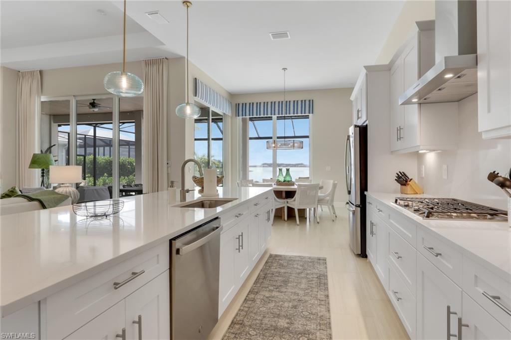 Kitchen with white cabinets, wall chimney range hood, light stone countertops, and pendant lighting