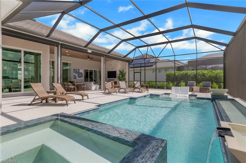 View of pool featuring a pool with connected hot tub, a patio, a sunroom, glass enclosure, and ceiling fan