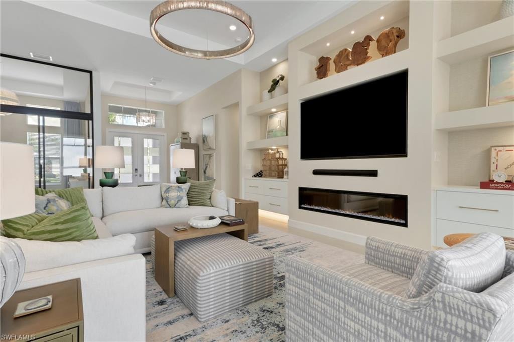 Living area with built in features, a glass covered fireplace, a raised ceiling, and french doors