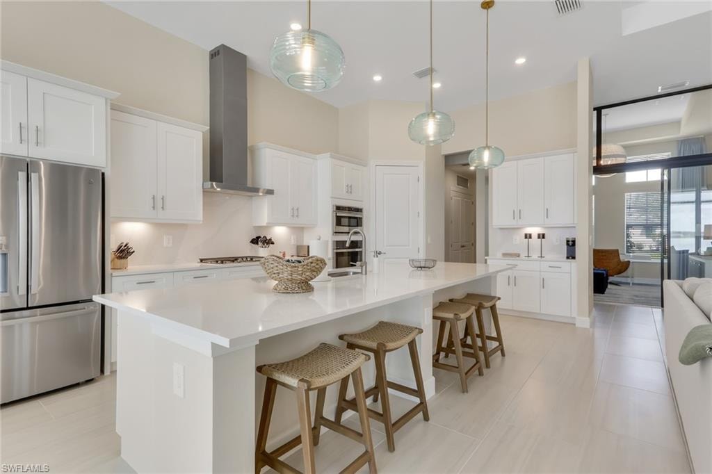 Kitchen with appliances with stainless steel finishes, a kitchen breakfast bar, a large island with sink, white cabinets, and wall chimney exhaust hood