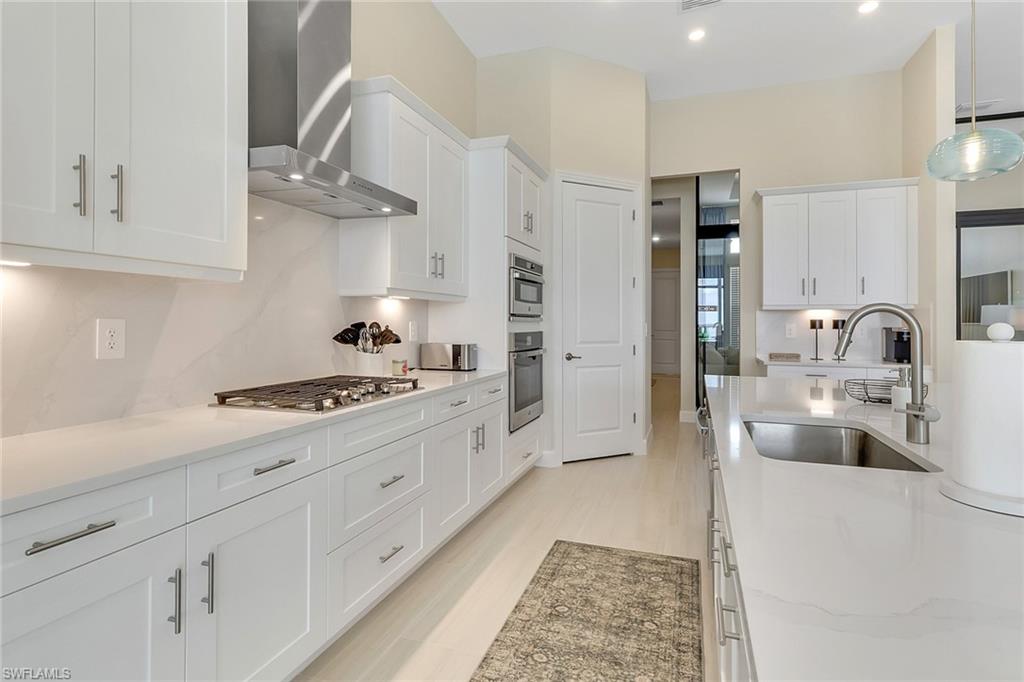 Kitchen featuring hanging light fixtures, white cabinetry, wall chimney exhaust hood, light stone countertops, and recessed lighting