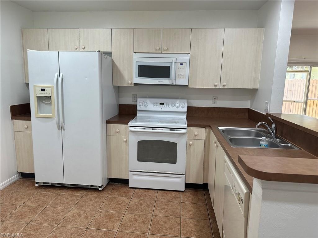 Kitchen featuring kitchen peninsula, sink, white appliances, and light tile patterned floors