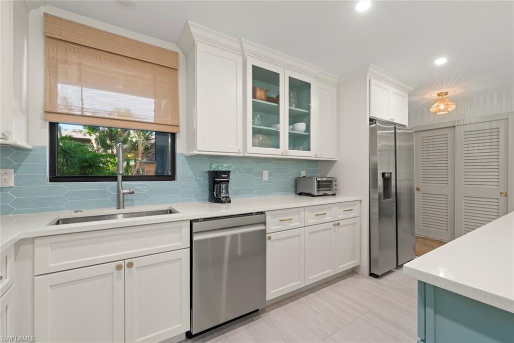 Kitchen featuring appliances with stainless steel finishes, white cabinetry, light stone counters, glass insert cabinets, and recessed lighting