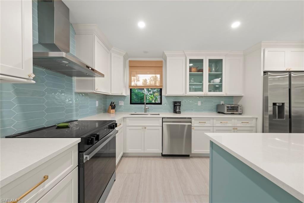 Kitchen featuring stainless steel appliances, wall chimney range hood, white cabinets, light stone countertops, and recessed lighting