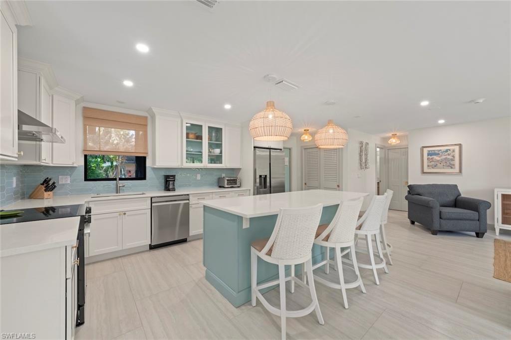 Kitchen featuring open floor plan, appliances with stainless steel finishes, a kitchen island, a kitchen bar, and pendant lighting