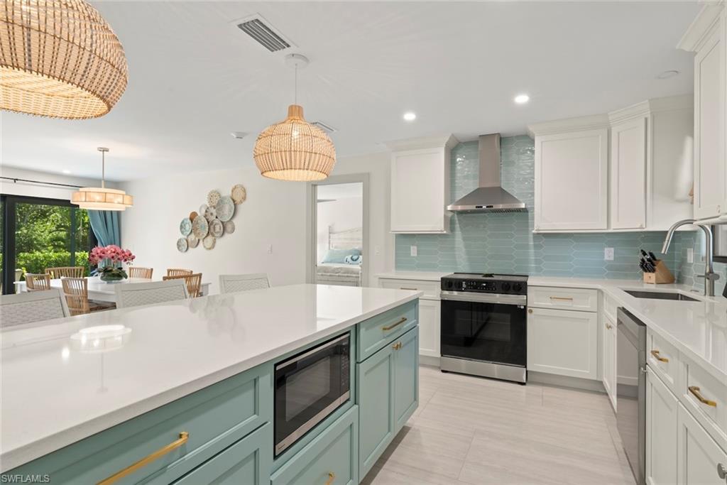 Kitchen featuring appliances with stainless steel finishes, pendant lighting, white cabinets, wall chimney range hood, and recessed lighting