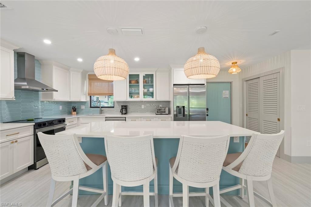 Kitchen featuring appliances with stainless steel finishes, a center island, wall chimney exhaust hood, white cabinets, and tasteful backsplash