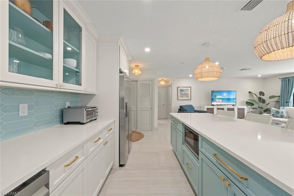 Kitchen with white cabinetry, light stone counters, open floor plan, glass insert cabinets, and recessed lighting