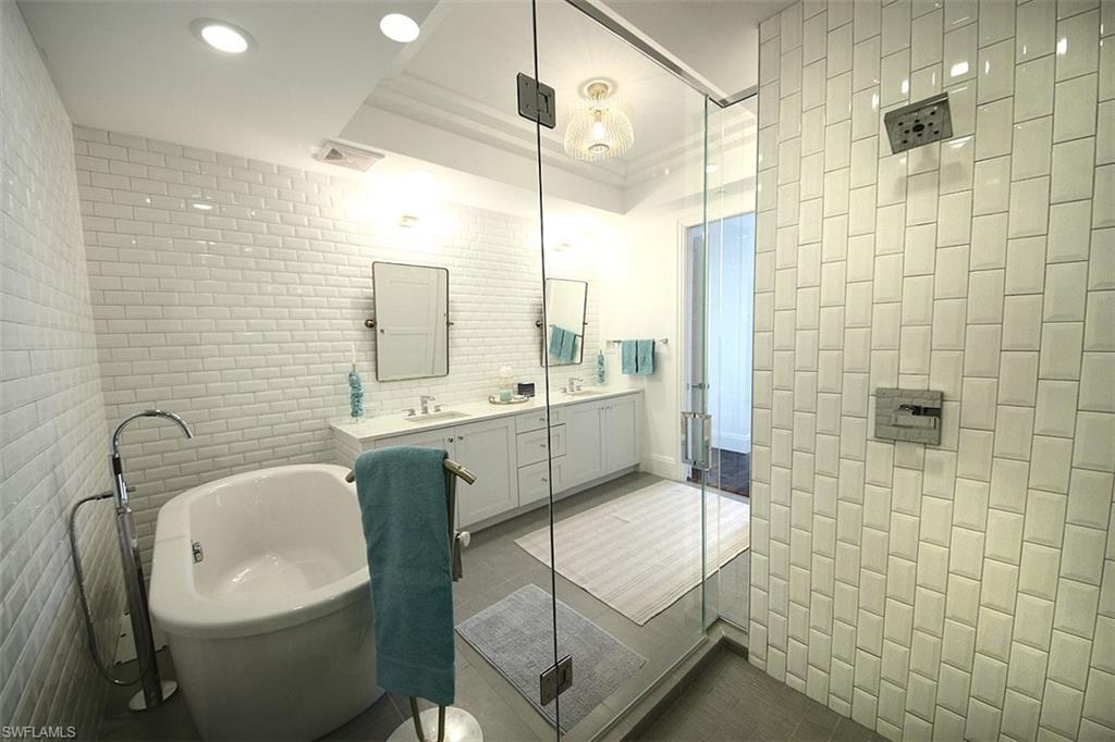 Full bathroom featuring tile walls, double vanity, a soaking tub, dark tile patterned flooring, and a shower with door