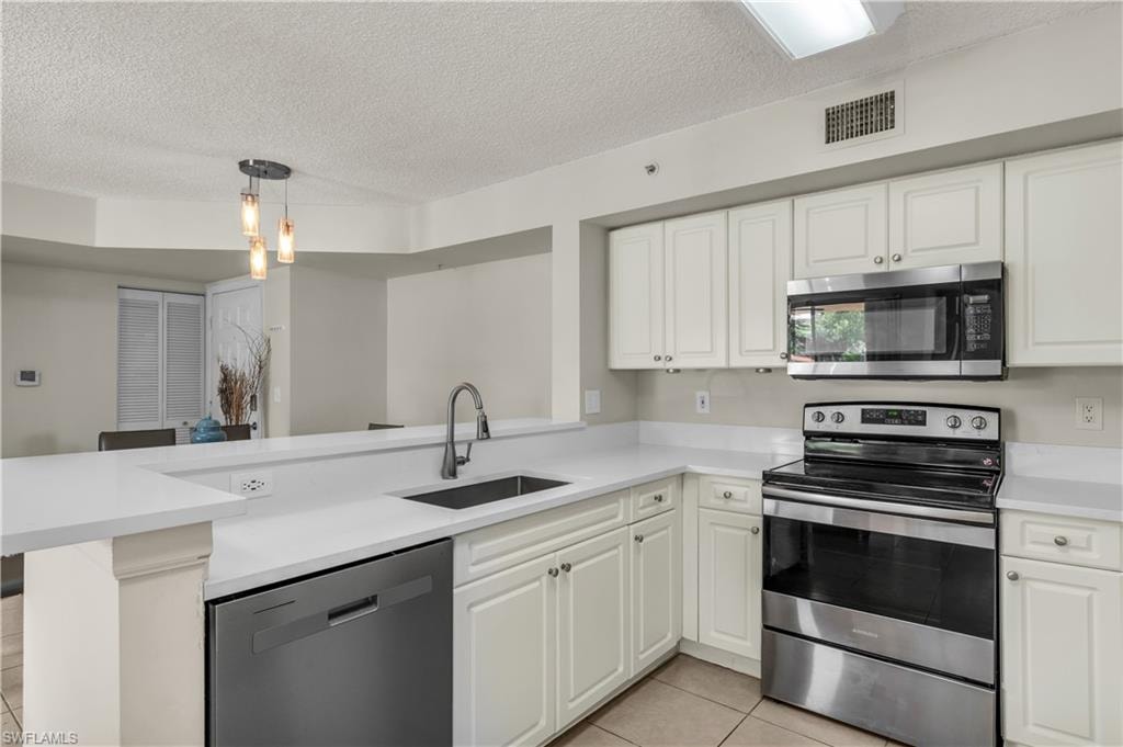 Kitchen with stainless steel appliances, light tile patterned flooring, a textured ceiling, white cabinetry, and pendant lighting