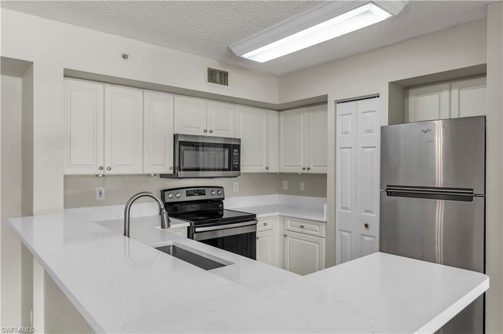 Kitchen featuring appliances with stainless steel finishes, a textured ceiling, white cabinetry, light stone counters, and a peninsula