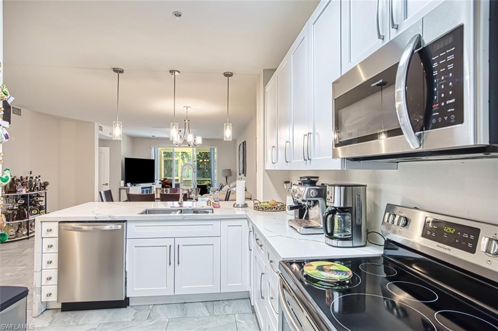 Kitchen featuring stainless steel appliances, white cabinetry, hanging light fixtures, a peninsula, and light stone counters
