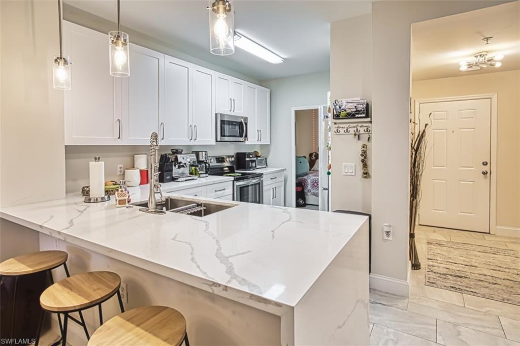 Kitchen featuring light marble finish floors, a peninsula, stainless steel appliances, a breakfast bar area, and white cabinetry