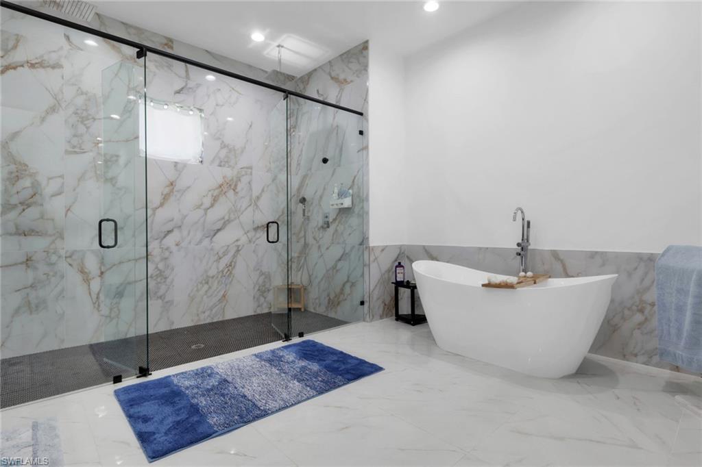 Full bathroom featuring tile walls, marble tiled floors, a wainscoted wall, a freestanding tub, and a marble finish shower
