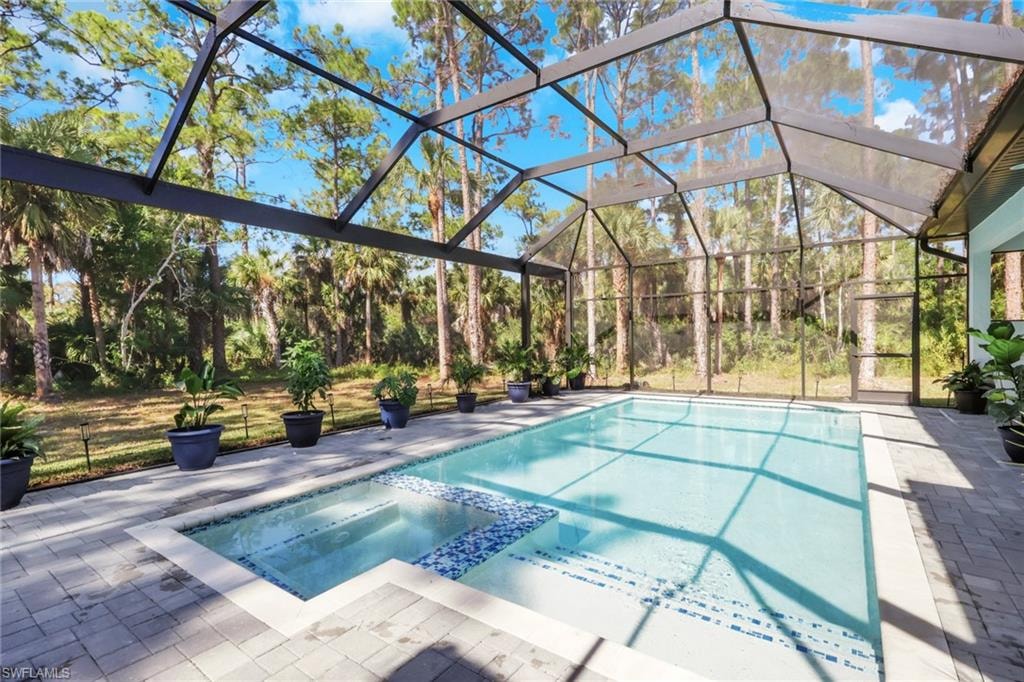 View of pool featuring glass enclosure, a pool with connected hot tub, a sunroom, and a patio