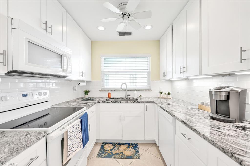 Kitchen with white appliances, white cabinetry, light tile patterned floors, recessed lighting, and light stone counters