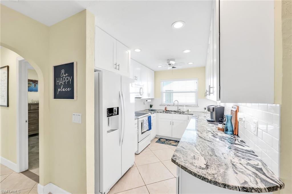 Kitchen featuring light stone countertops, white appliances, arched walkways, white cabinetry, and recessed lighting
