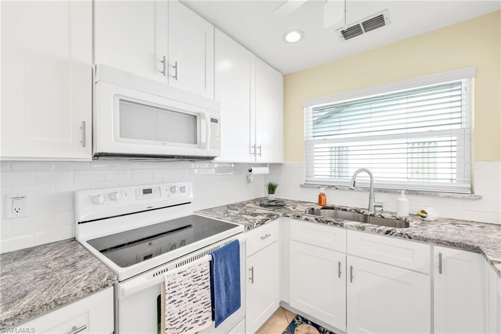 Kitchen featuring white appliances, white cabinets, light stone counters, tasteful backsplash, and recessed lighting