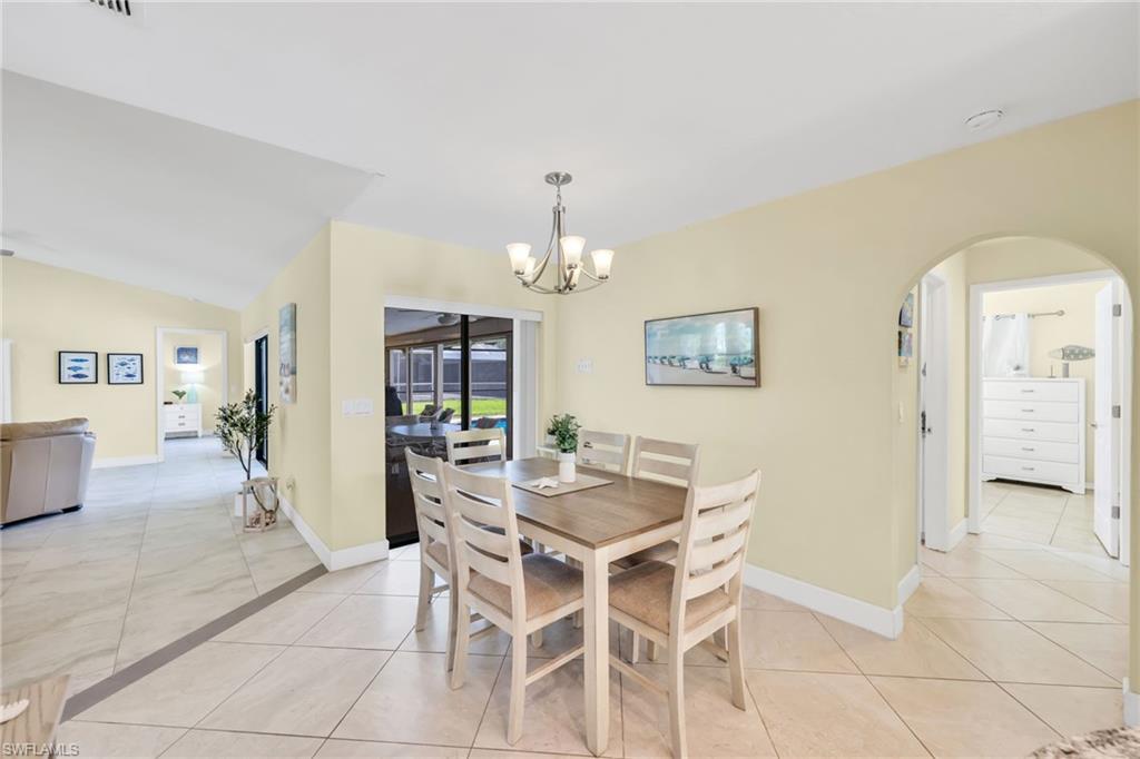 Dining space with light tile patterned floors, arched walkways, a chandelier, and vaulted ceiling