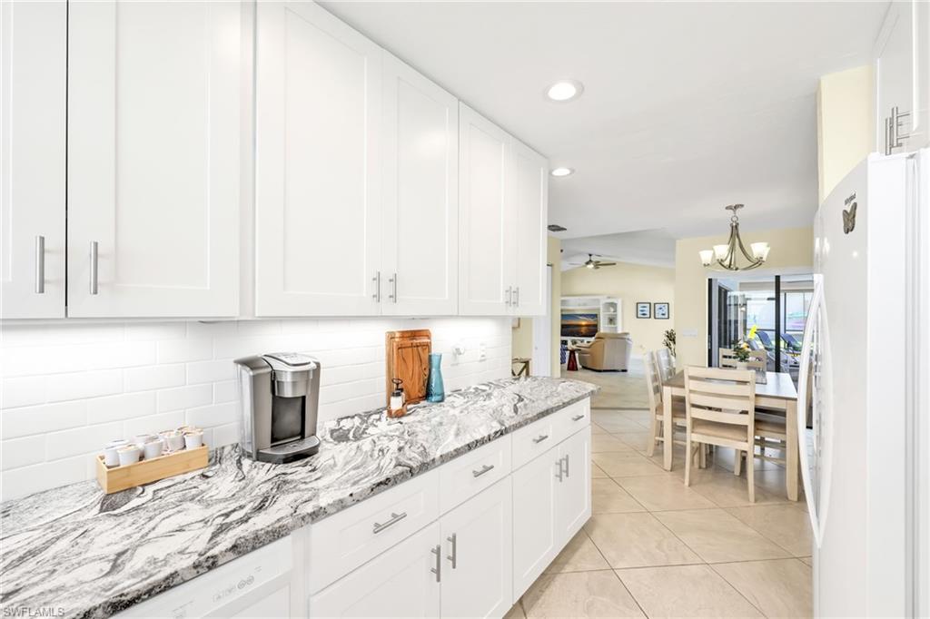 Kitchen with white cabinets, freestanding refrigerator, decorative backsplash, light stone countertops, and recessed lighting