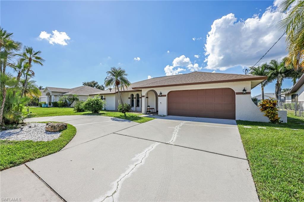 Single story home featuring a front lawn, driveway, stucco siding, and an attached garage