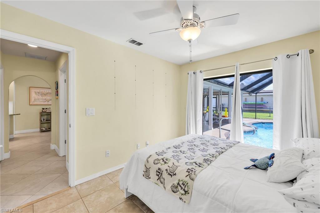 Bedroom with access to outside, light tile patterned flooring, arched walkways, and ceiling fan