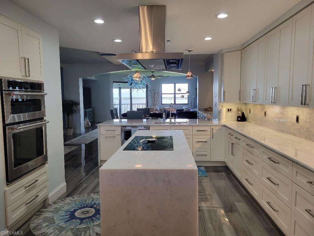 Kitchen with white cabinets, decorative backsplash, a peninsula, a kitchen island, and light stone counters