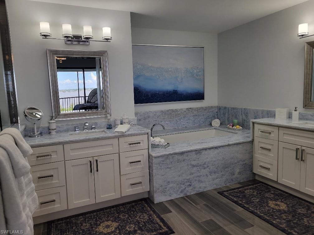 Full bath with two vanities, a garden tub, and dark wood-style floors
