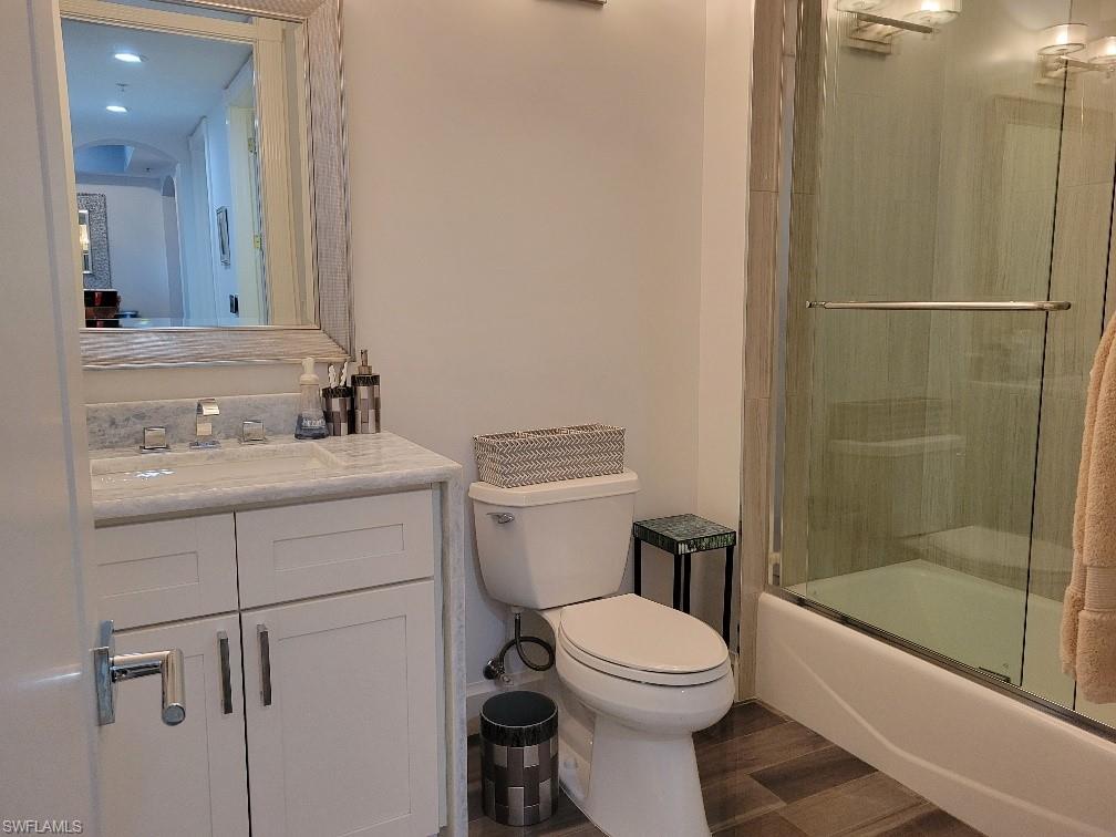 Full bathroom with vanity, dark wood-style floors, and enclosed tub / shower combo